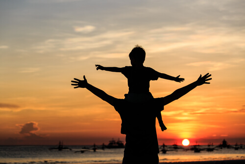 Hijo aprendiendo sobre los hombros de su padre en la playa