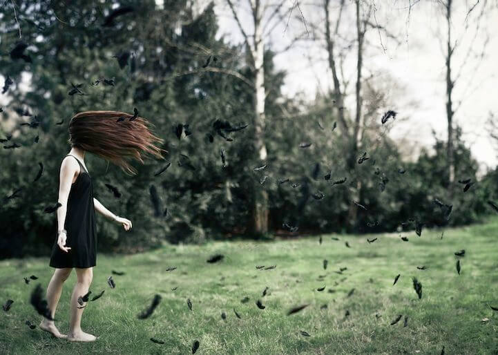 Mujer caminando entre plumas negras sin llegar a alcanzar la felicidad