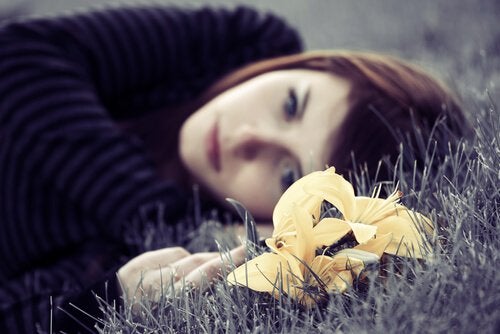 Eftertænksom kvinde ligger på græs med blomst i hånden efter at have set The Shift