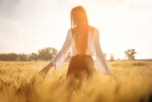 Kobieta spacerująca po złotym polu w słoneczny dzień.