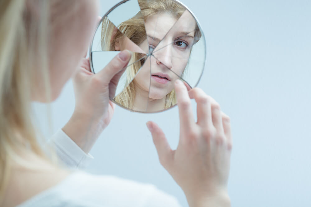 Mujer mirándose en espejo roto