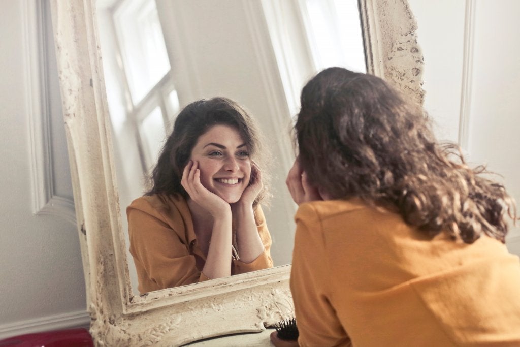 Uśmiechnięta kobieta patrząca na swoje odbicie w lustrze