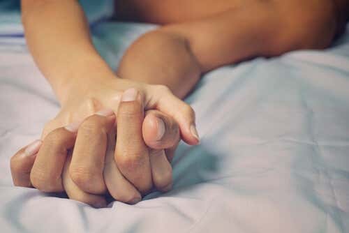 A couple holding hands while being intimate in bed.