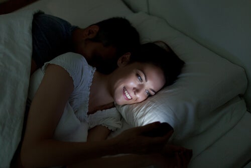 Chica revisando su móvil mientras su pareja duerme