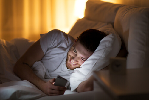 Glimlachende man die naar mobiel kijkt, wat neerkomt op lange-afstandsrealisaties.