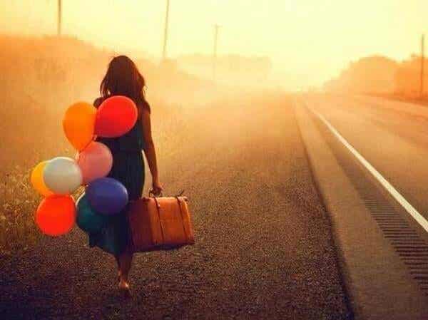 Mujer caminando con una maleta y globos de colores