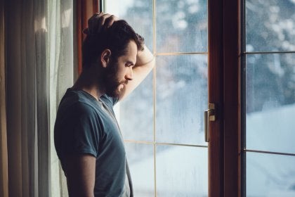 Hombre triste cerca de la ventana pensando en las heridas que deja la infidelidad 
