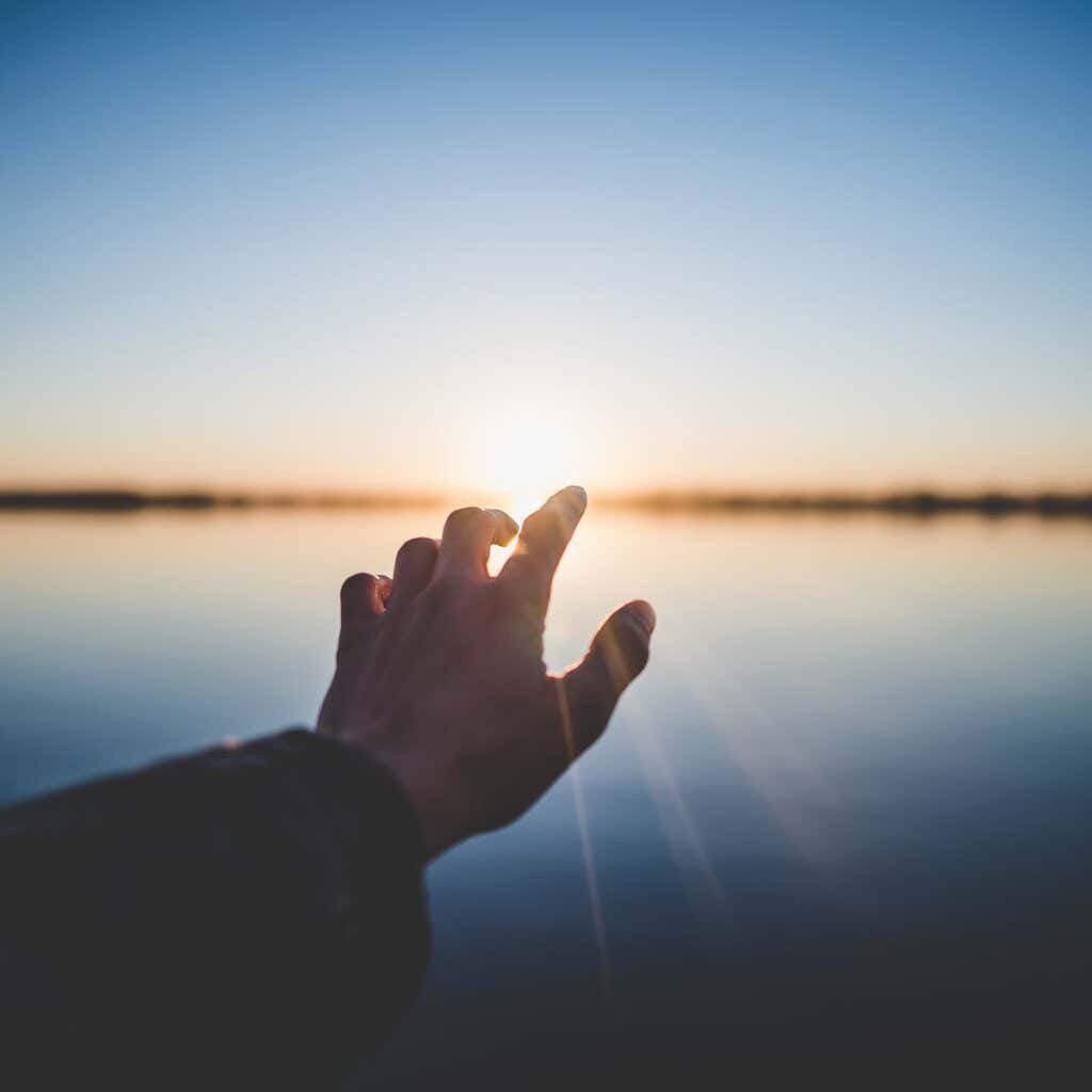 Käsi osoittaa auringonlaskua.