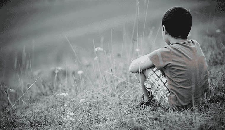 niño de espaldas sentado pensando en ser feliz después de haber vivido una infancia traumática