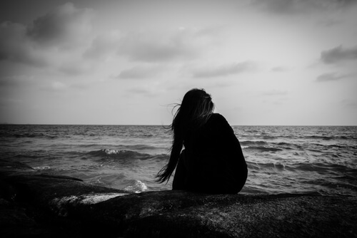 Mujer joven sola sentada encima de las rocas observando el mar