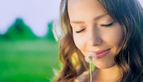 Happy woman thinking about the past while smelling a dandelion