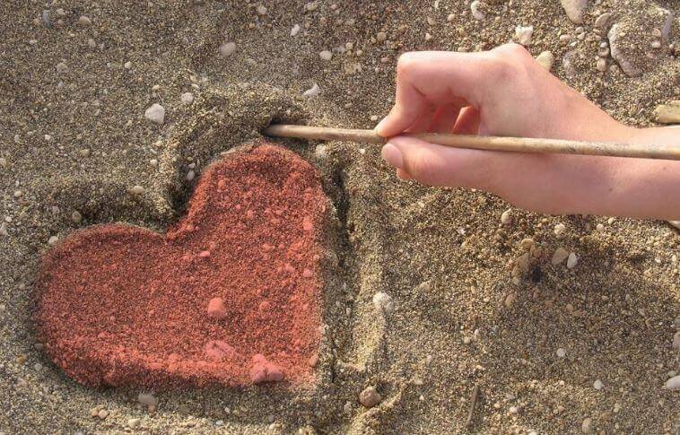 Mano dibujando un corazón en la arena simbolizando el arte de hacer el bien