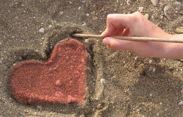 Mano dibujando un corazón en la arena simbolizando el arte de hacer el bien