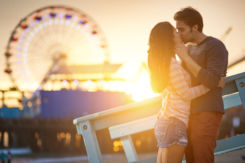 Pareja besándose cerca de una noria disfrutando de su amor