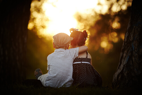 Niño sentado abrazando a niña al atardecer
