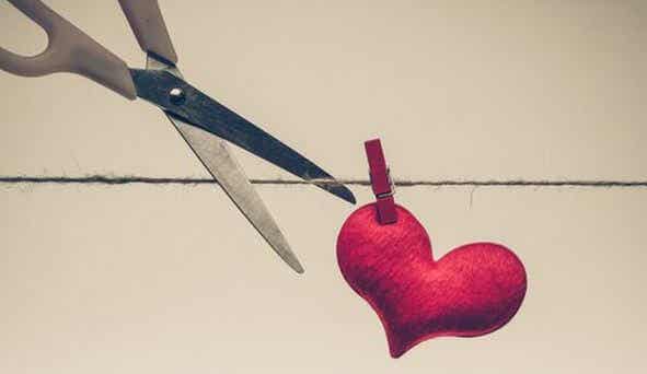 Corazón colgado de una cuerda mientras una tijera intenta cortarla