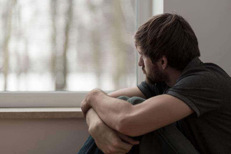 Hombre mirando por una ventana con fatiga emocional