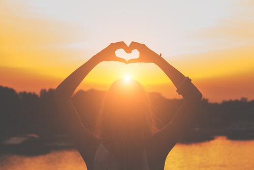 Manos haciendo un corazón al amanecer