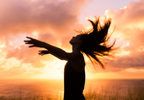 Mujer con los brazos arriba y el pelo suelto al atardecer