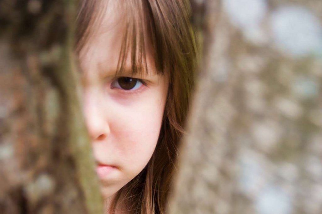 Cara de niña enfada detrás de un árbol