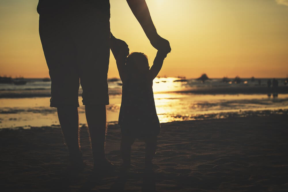 Padre agarrando las manos a su hijo en la playa