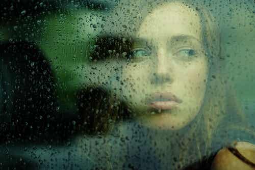 Mujer pensando detrás de una ventana con gotas de lluvia