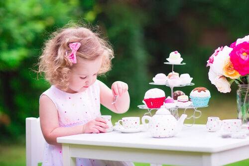 Niña estereotipo vestida de rosa jugando con tacitas