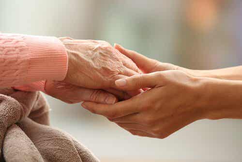 Joven agarrando las manos de una anciana con actitudes cariñosas