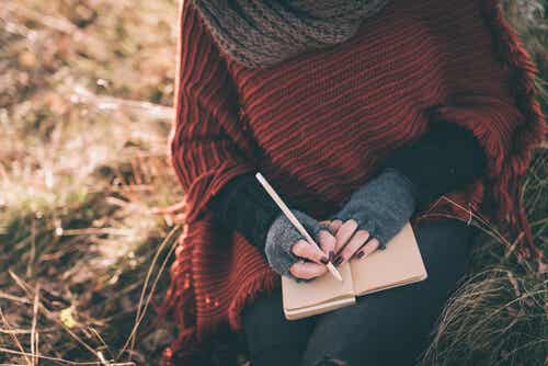 Naisen kädet kirjoittavat muistikirjaan kentällä
