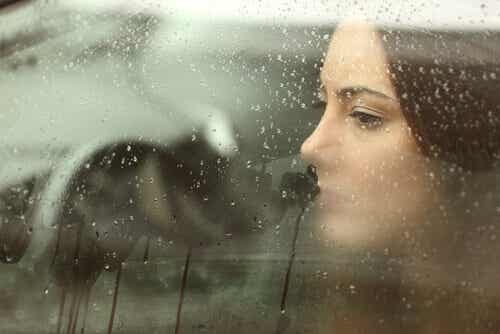 Mujer triste mirando por la ventana de su coche llena de gotas de agua y pensando en ciertos momentos