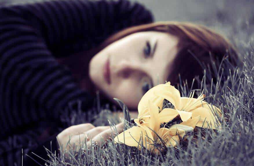 Mujer triste tumbada en el suelo con una flor amarilla