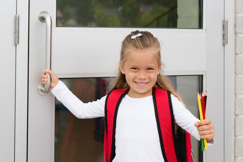 Niña entrando a la puerta del colegio con lápices en la mano
