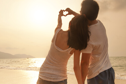 Pareja enamorada formando un corazón con sus manos en la playa