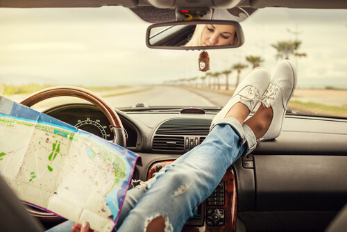 Piernas de una mujer sobre volante del coche con un mapa