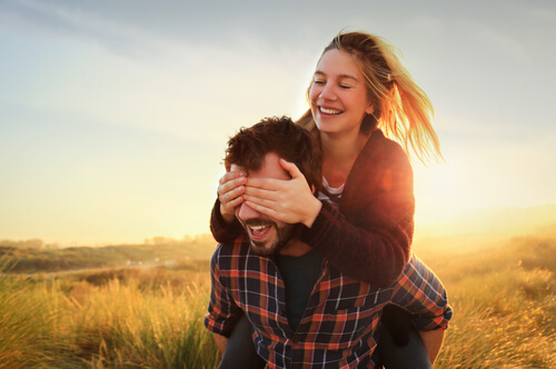 Chica subida en la espalda de su chico tapándole los ojos disfrutando de su amor