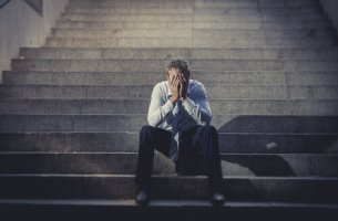 Hombre con las manos en la cara sentado en una escalera afectado por el desempleo