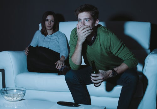 Mujer enfadada sentada en el sillón mientras su pareja ve el futbol