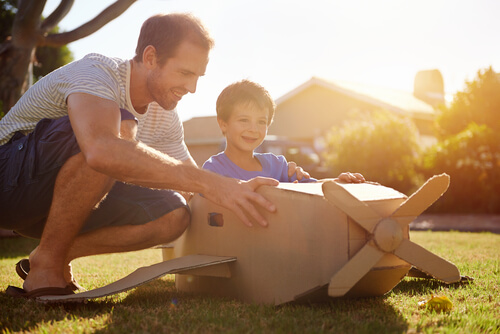 Niño montado en un avión de cartón jugando con su padre