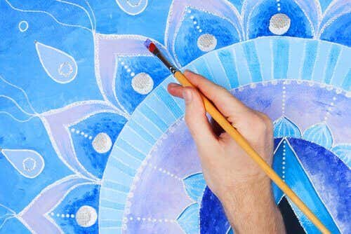 A hand painting a mandala with purple and blue tones.