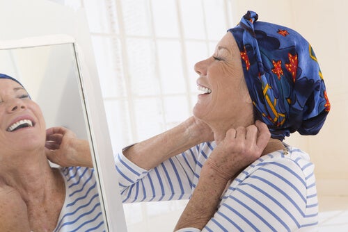Mujer con cáncer mirándose al espejo sonriendo mientras se pone su pañuelo en la cabeza