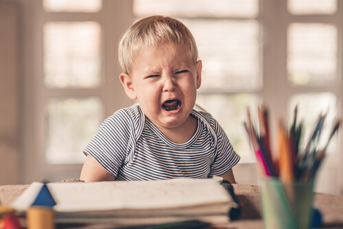 Niño llorando con una hoja y lápices sobre la mesa