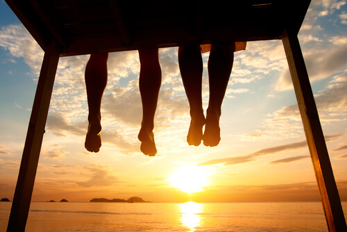 Piernas de amigos sentados viendo el atardecer