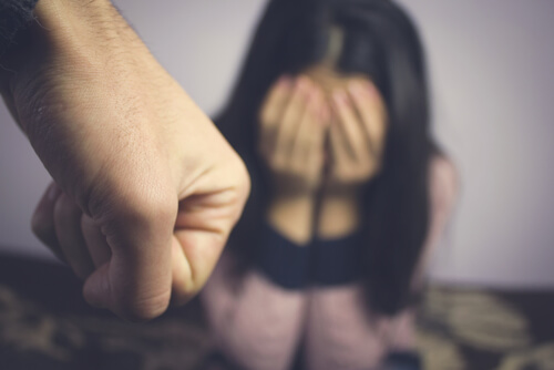 Puño de un hombre y una mujer sentada con miedo