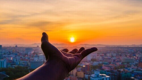 Mano señalando el sol al amanecer representando cómo afecta el cambio de hora durante el confinamiento