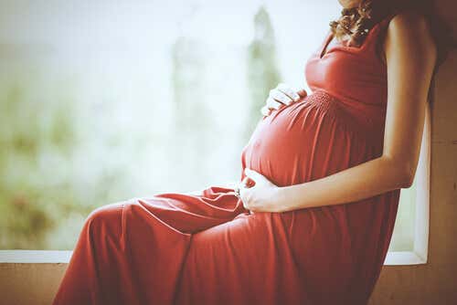 Mujer embarazada con un vestido rojo sujetándose la barriga