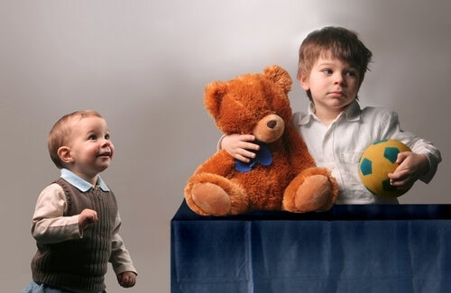Niño agarrando un oso y un balón sin compartirlo con su hermano