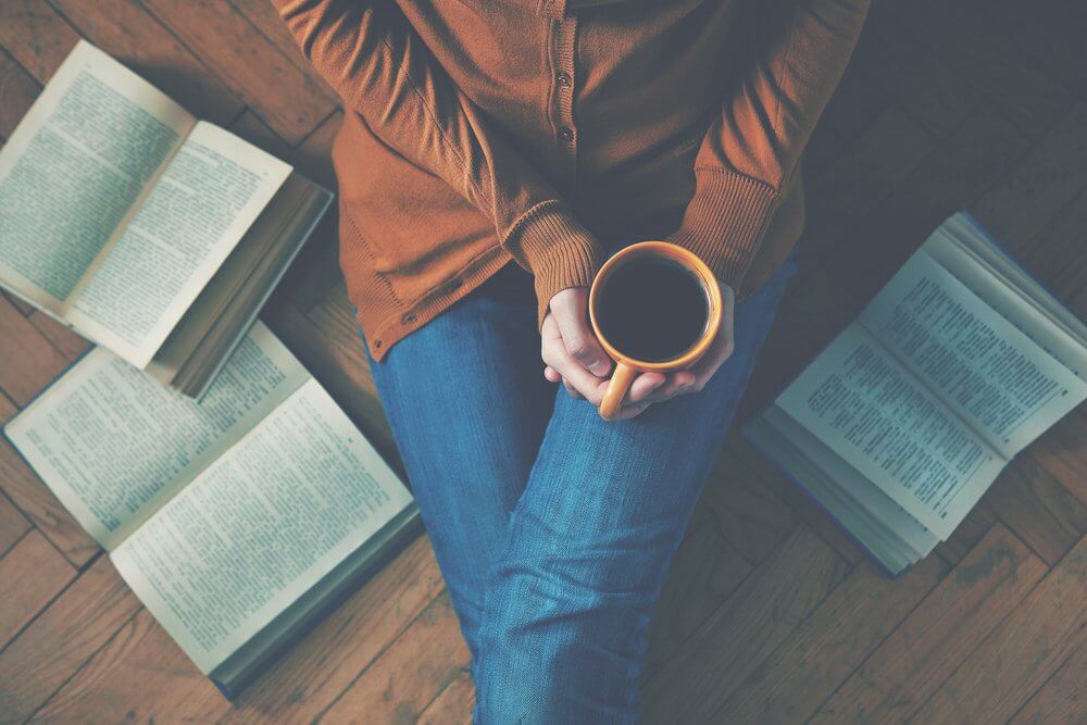 Mujer tomando café rodeada de libros
