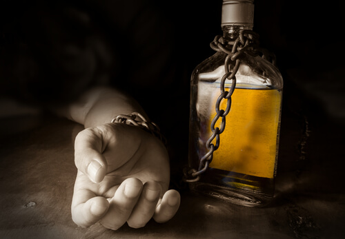 Mano encadenada a una botella de alcohol