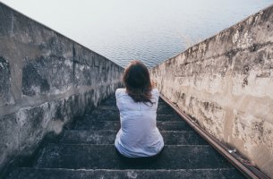 Mujer mirando al mar sentada en una escalera