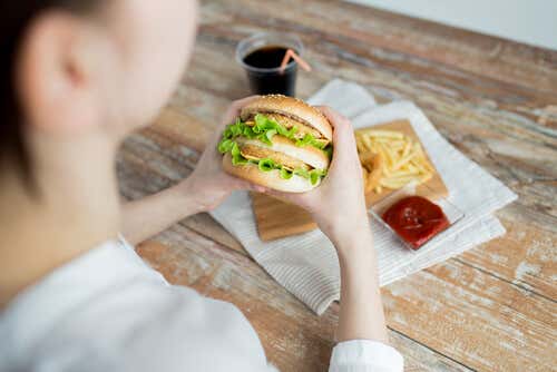 Mujer comiendo una hamburguesa por problemas de alimentación emocional